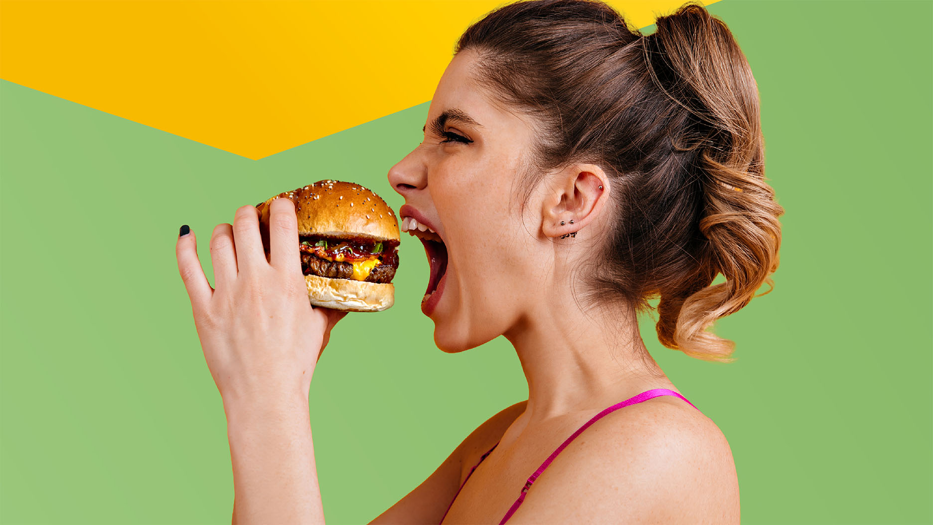 Giovane donna morde con gioia in un succoso hamburger (con un elemento di design giallo sopra)