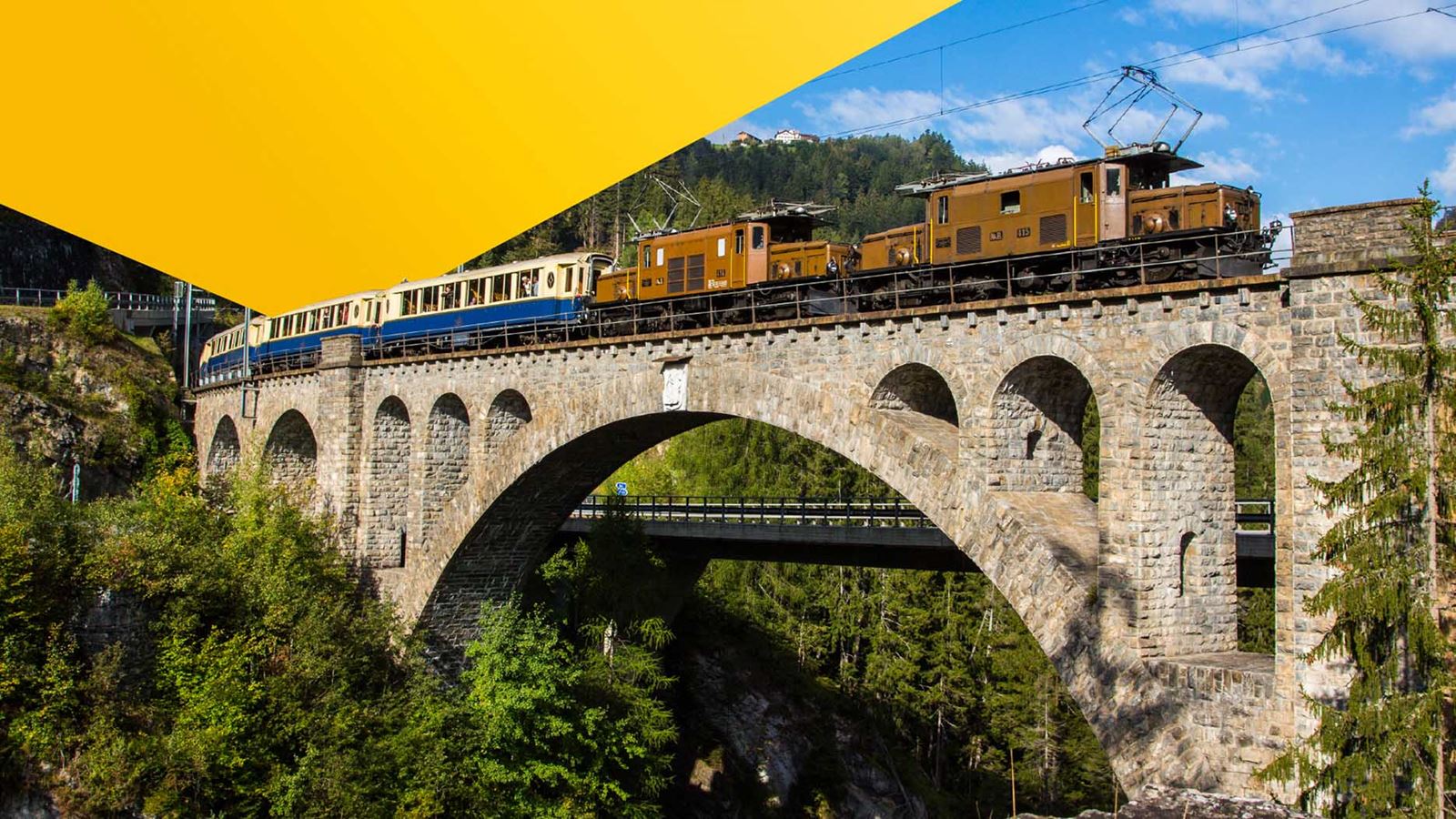 Eine Krokodil-Lok zieht die geschichtsträchtigen Pullman-Waggons auf der Glacier-Express-Route (mit überliegendem gelbem Designelement)