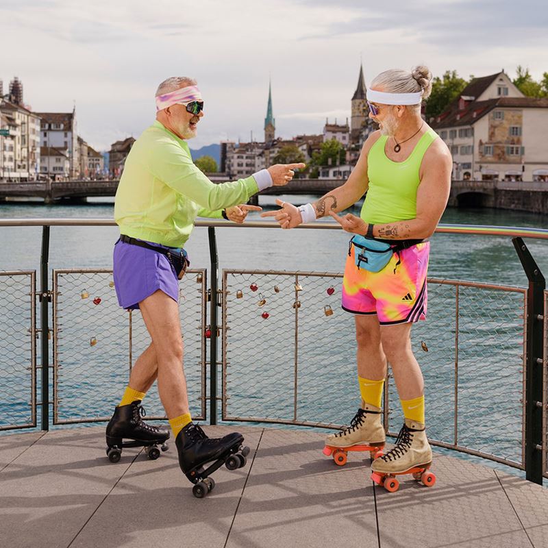 Zwei ältere Herren in Neon-Kleidern auf Rollerskates an einem Fluss