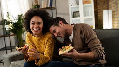 Deux personnes mangent ensemble une pizza sur le canapé