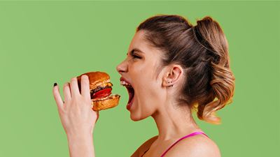 Junge Frau beisst mit Vorfreude in einen saftigen Burger